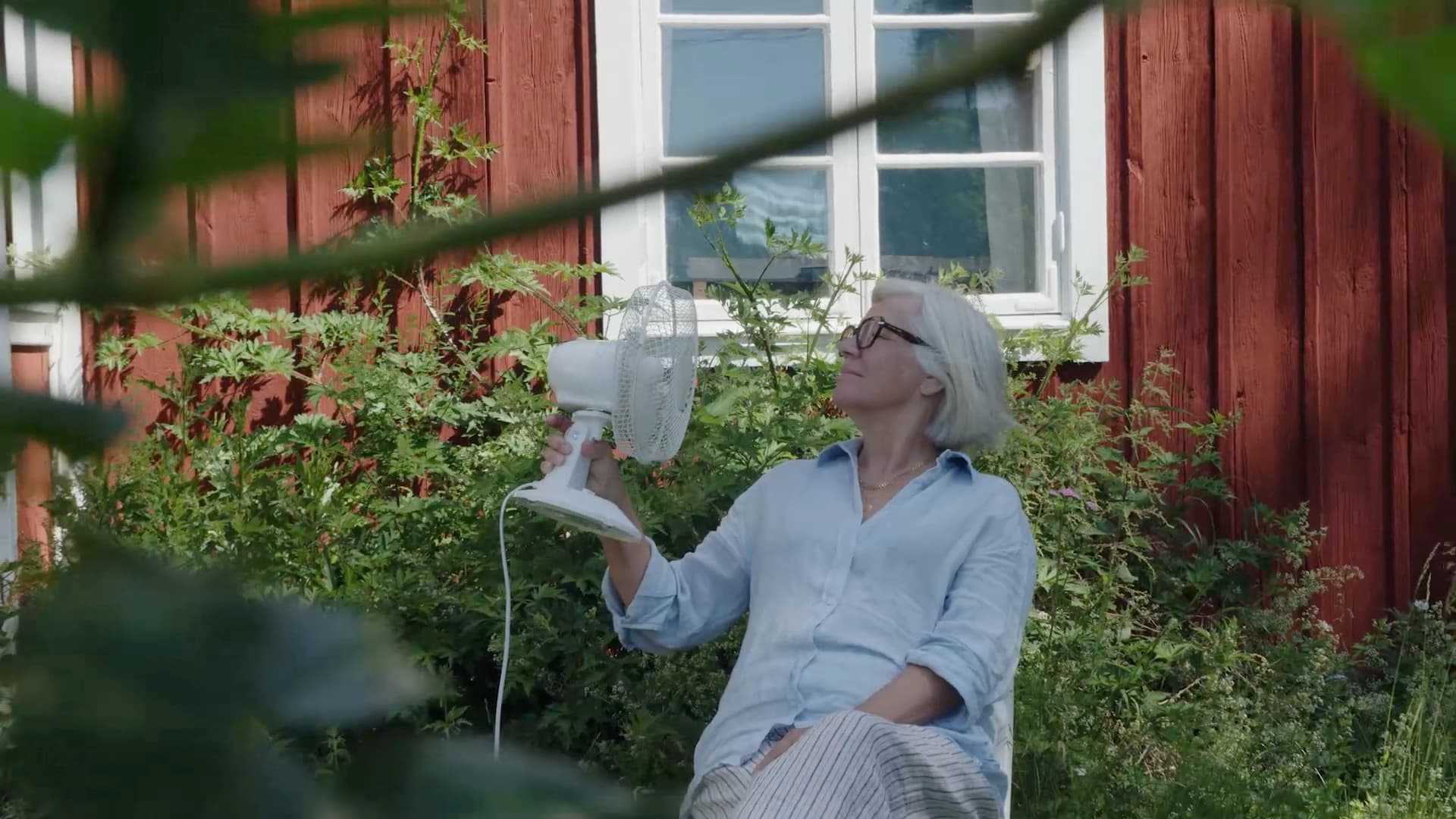 Äldre Elvy-kund som svalkar sig med en bordsfläkt utanför ett rött hus
