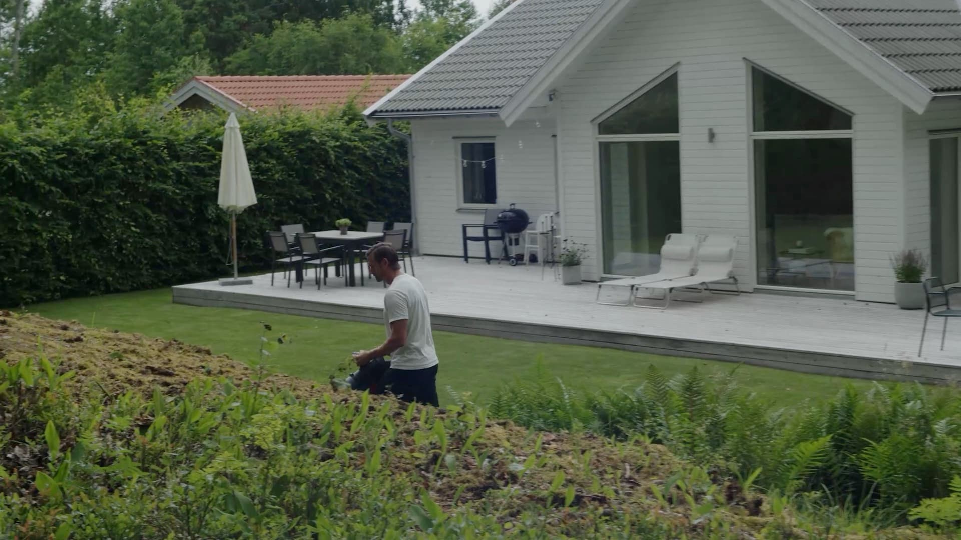 Man med lövblås på gräsmattan vid en vit villa med altan