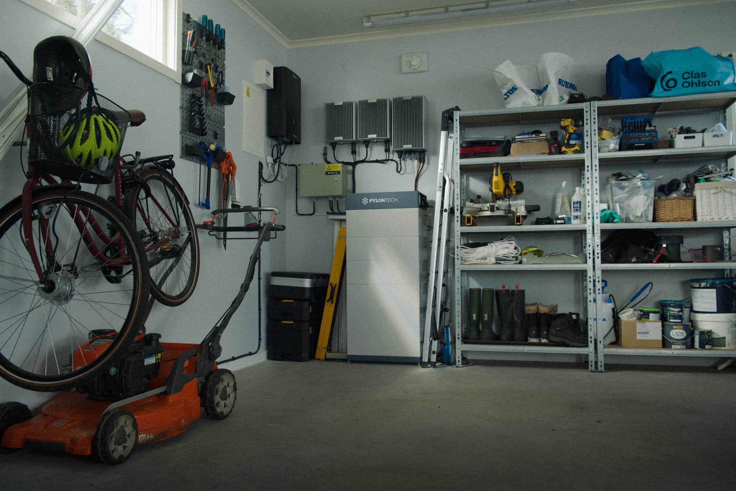 Hembatteri och växelriktare i ett garage, bredvid hyllor med verktyg